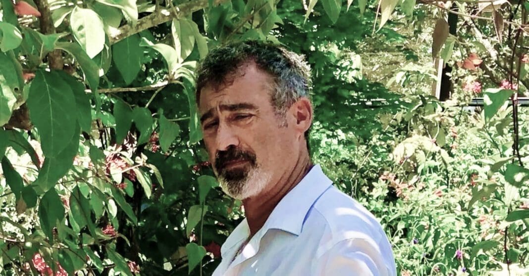 A man with a beard and mustache standing in front of trees.