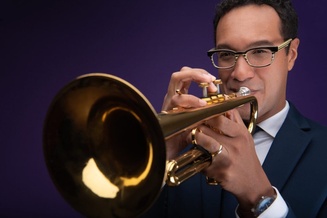 A man playing the trumpet in front of purple background.