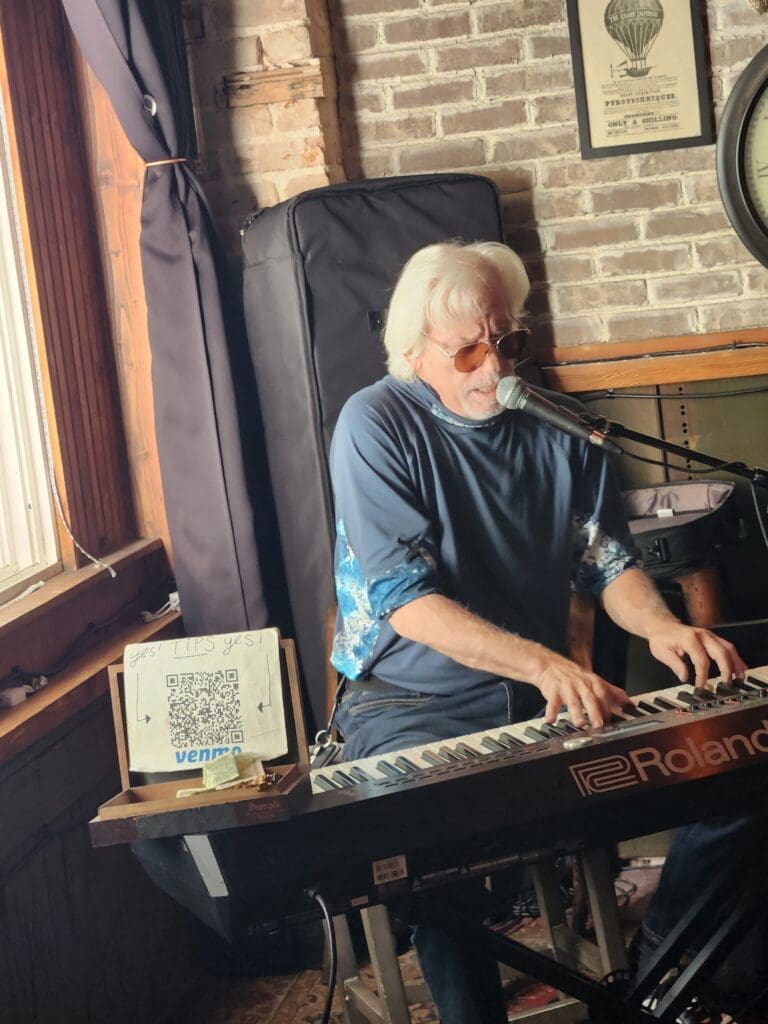 A man playing the piano in front of a brick wall.