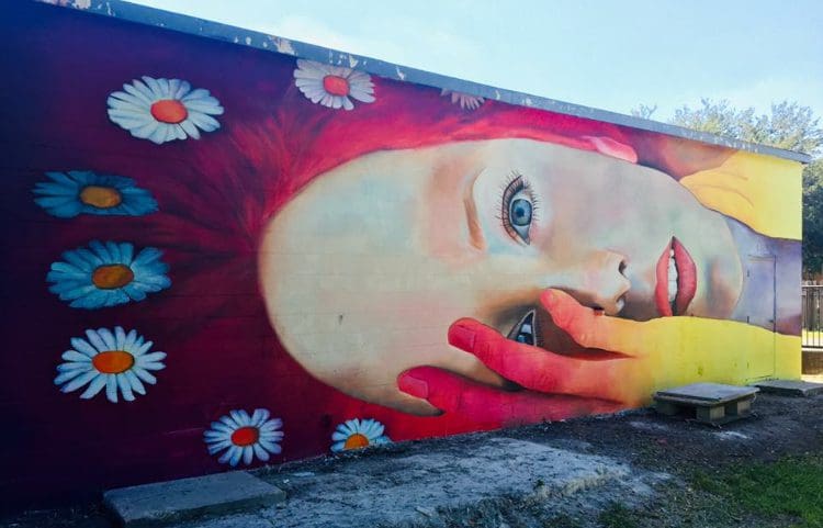 A mural of a woman 's face with hands and flowers on it.