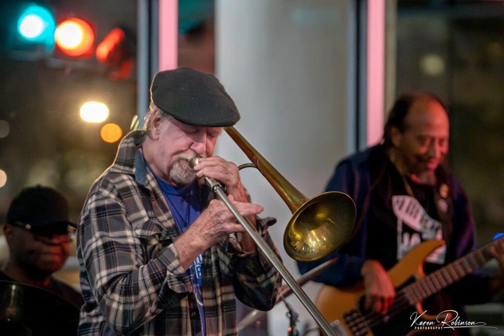 A man playing trombone with other musicians in the background.