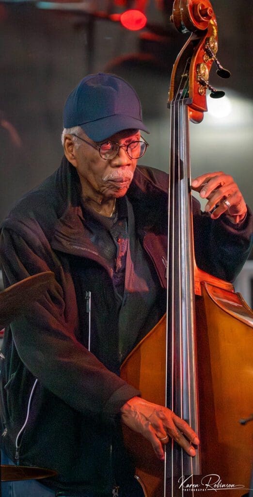 A man with glasses and hat on playing the bass.