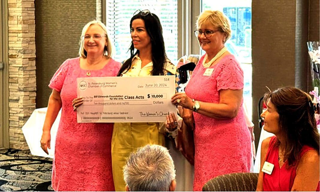 Three women in pink holding a large check.