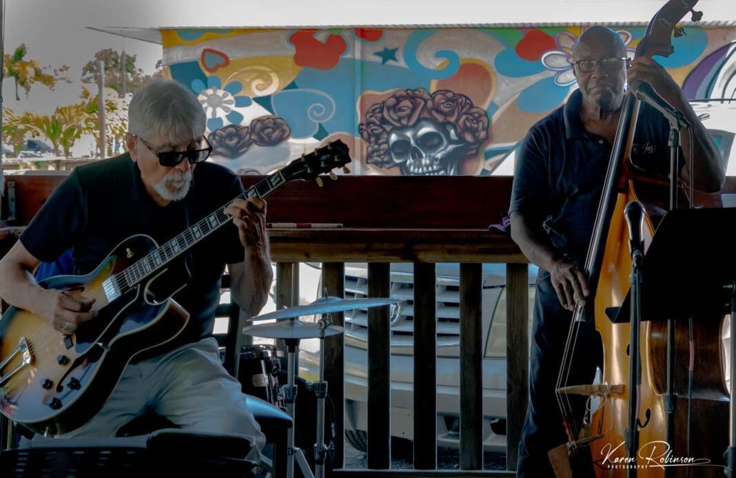 Two men playing instruments in front of a colorful wall.